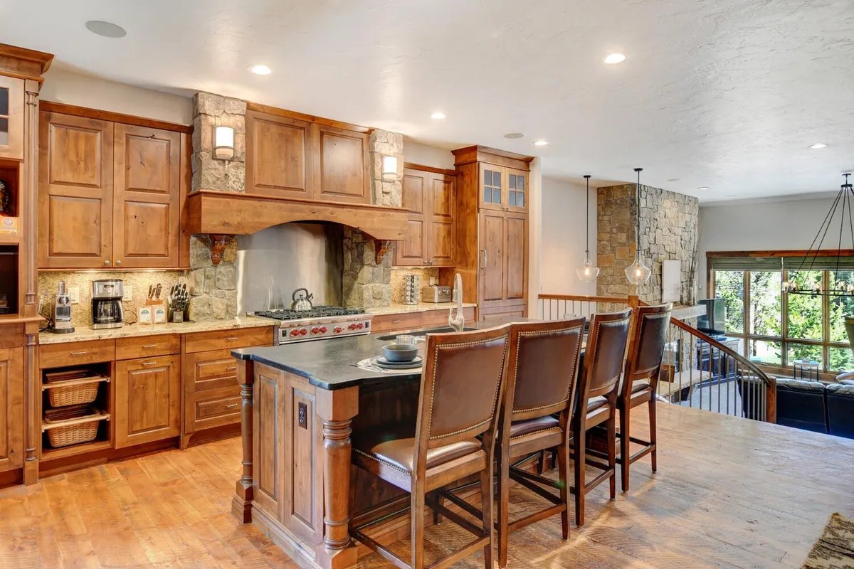 A chef-inspired kitchen with a prominent central island, custom wood cabinetry, and sleek stainless steel appliances, including a Wolf gas range. The stone backsplash and inviting layout make it a hub for cooking, entertaining, and sharing stories over meals.