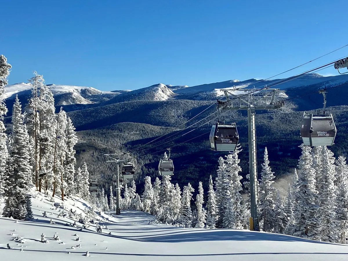 This invigorating exterior shot features ski lift gondolas gliding over snow-laden trees with expansive mountain ranges in the background. The scene conveys both the accessibility of ski-in/ski-out living and the breathtaking alpine setting, inviting guests to experience the thrill of the slopes and the serenity of the landscape.