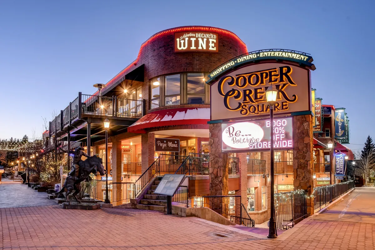 The lively exterior of Cooper Creek Square with prominent signage, a wine shop, a staircase, and a horse statue, set in an inviting environment ideal for shopping, dining, and socializing.