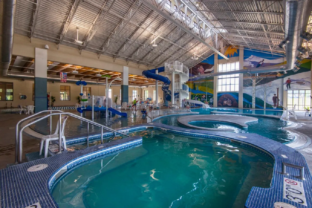 This image showcases an energetic indoor swimming pool with water slides, children playing, and multiple seating areas. The joyful and busy atmosphere captures families bonding and enjoying resort-style amenities together.