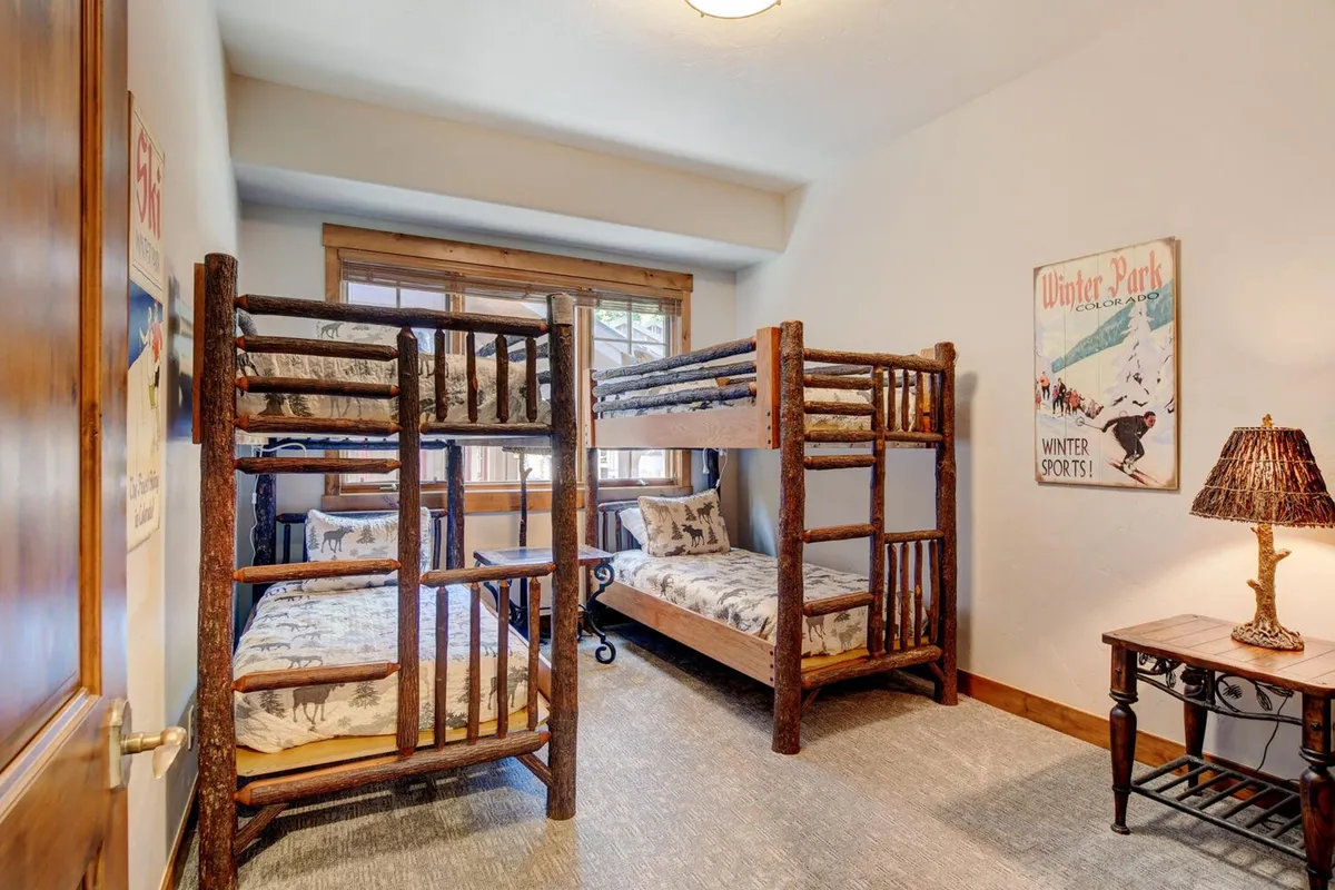 A fun and family-friendly bunk room with sturdy bunk beds, a colorful rug, lamp, wall art, and a window letting in natural light. The space feels playful and cozy, ideal for children or group stays.