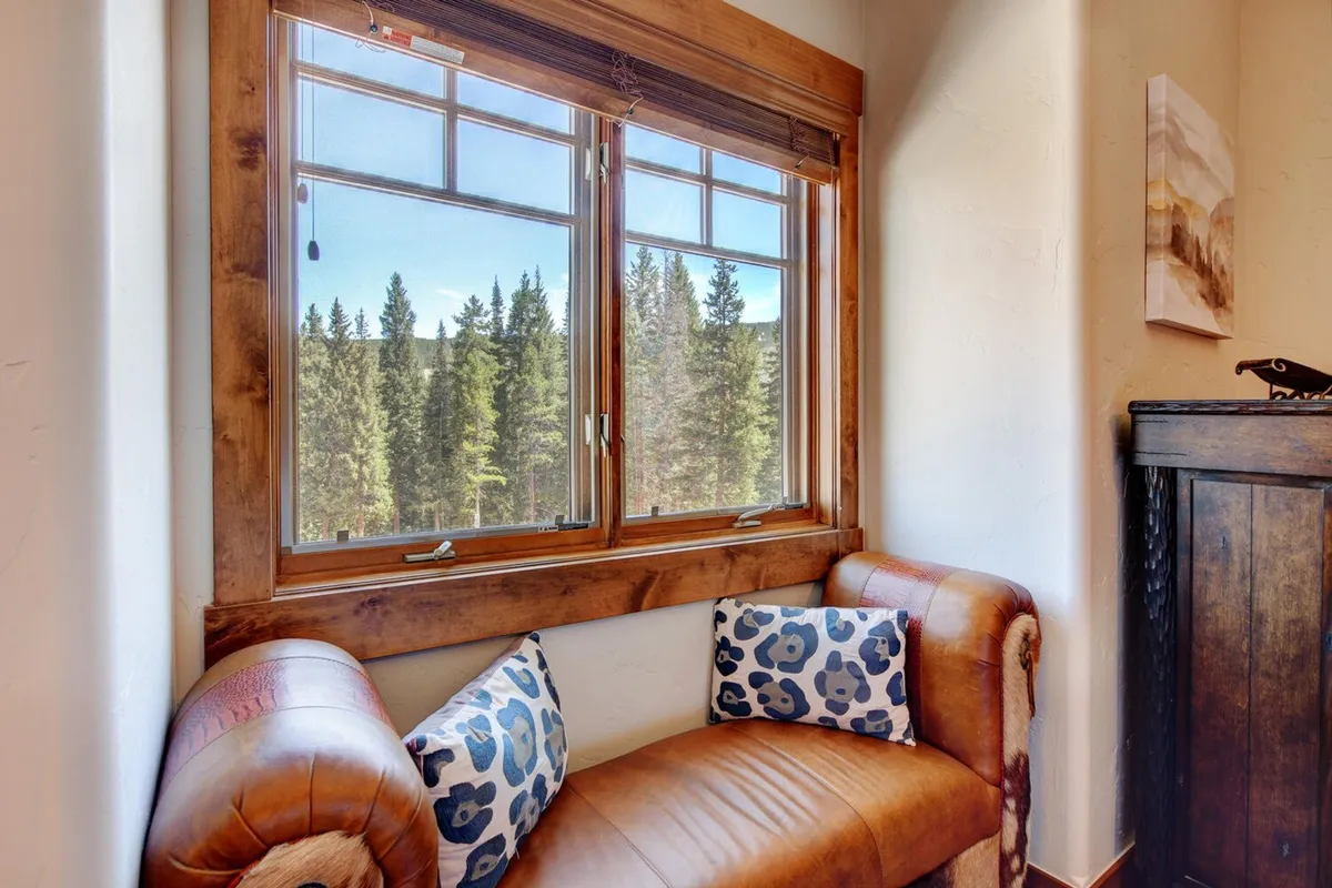 A cozy window seat with a leather bench and decorative pillows overlooks scenic mountain views, inviting guests to relax and take in the tranquil beauty outside. Soft, natural light fills the space, suggesting moments of peaceful reflection.