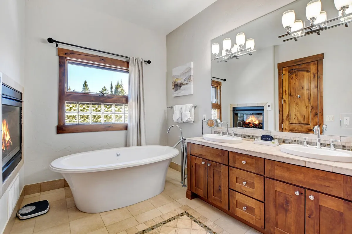 A spa-like bathroom featuring a freestanding tub, double vanity, fireplace, and large window providing natural light. The atmosphere is tranquil and inviting, perfect for relaxation and self-care rituals.