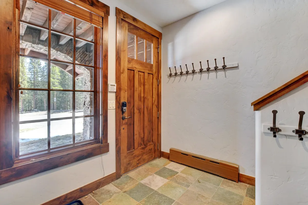 A welcoming entryway with a front door, large window letting in natural light, coat hooks, a staircase, and space where family members gather belongings before heading out. The scene is functional and inviting, suggesting ease of transition from indoor comfort to outdoor adventures.